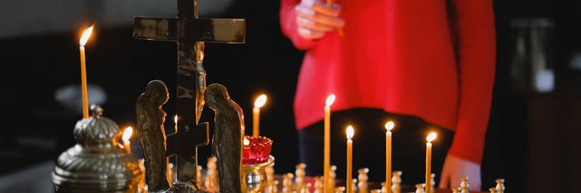 A woman lighting candles at an Orthodox altar with cross and statues in a church.