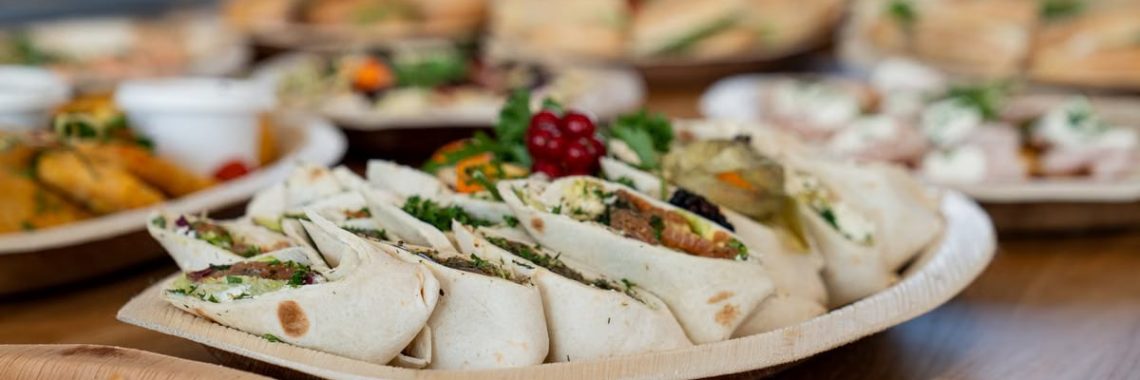 A wooden platter of assorted vegetarian wraps with fresh ingredients, perfect for parties.