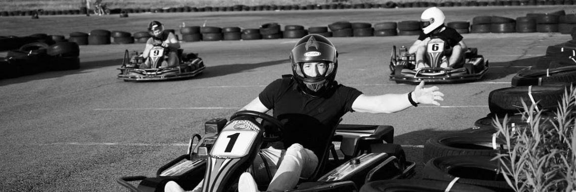 Black and white photo of people racing go-karts on an outdoor track.